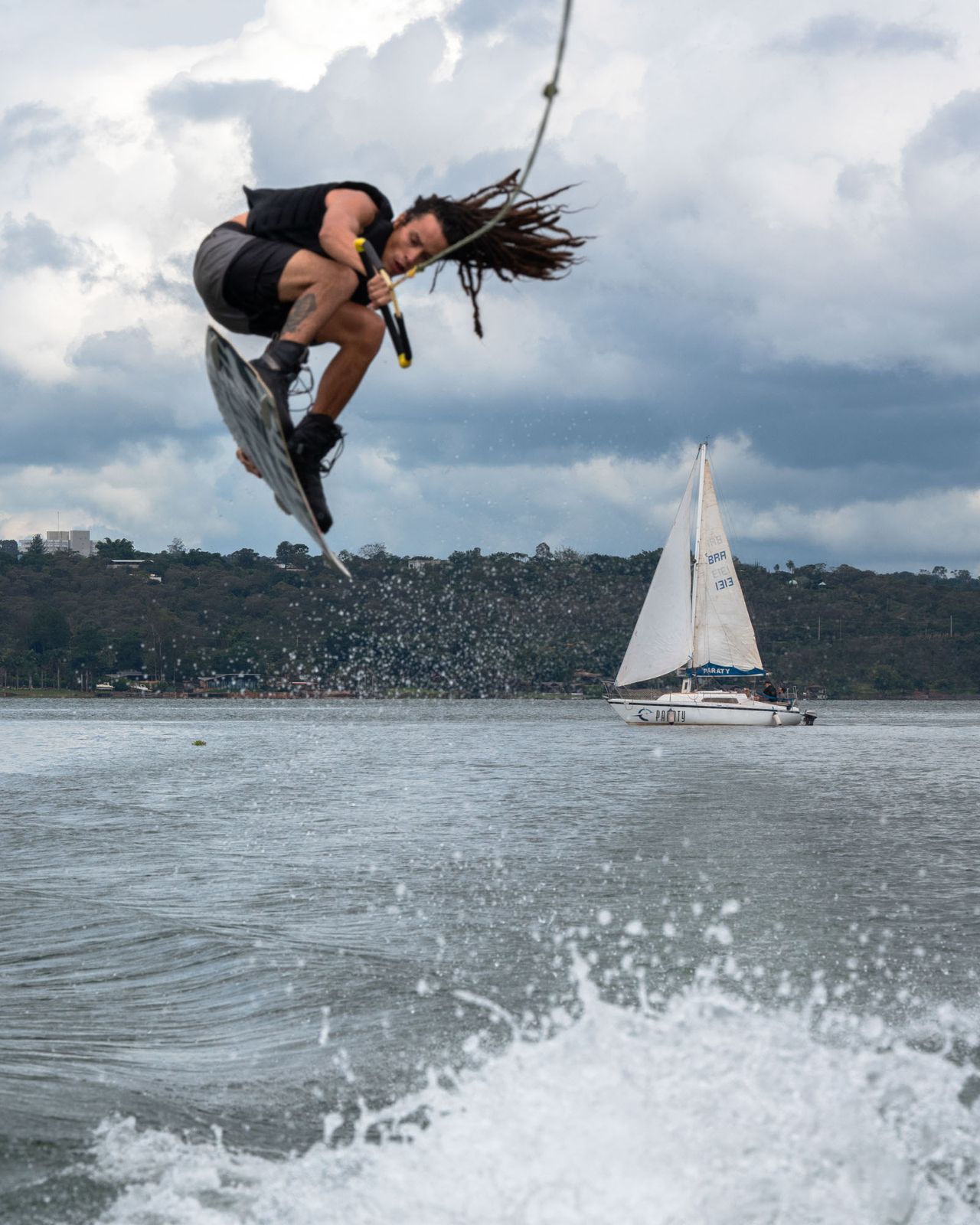 Wakeboarder no ar com veleiro ao fundo no Lago Paranoá