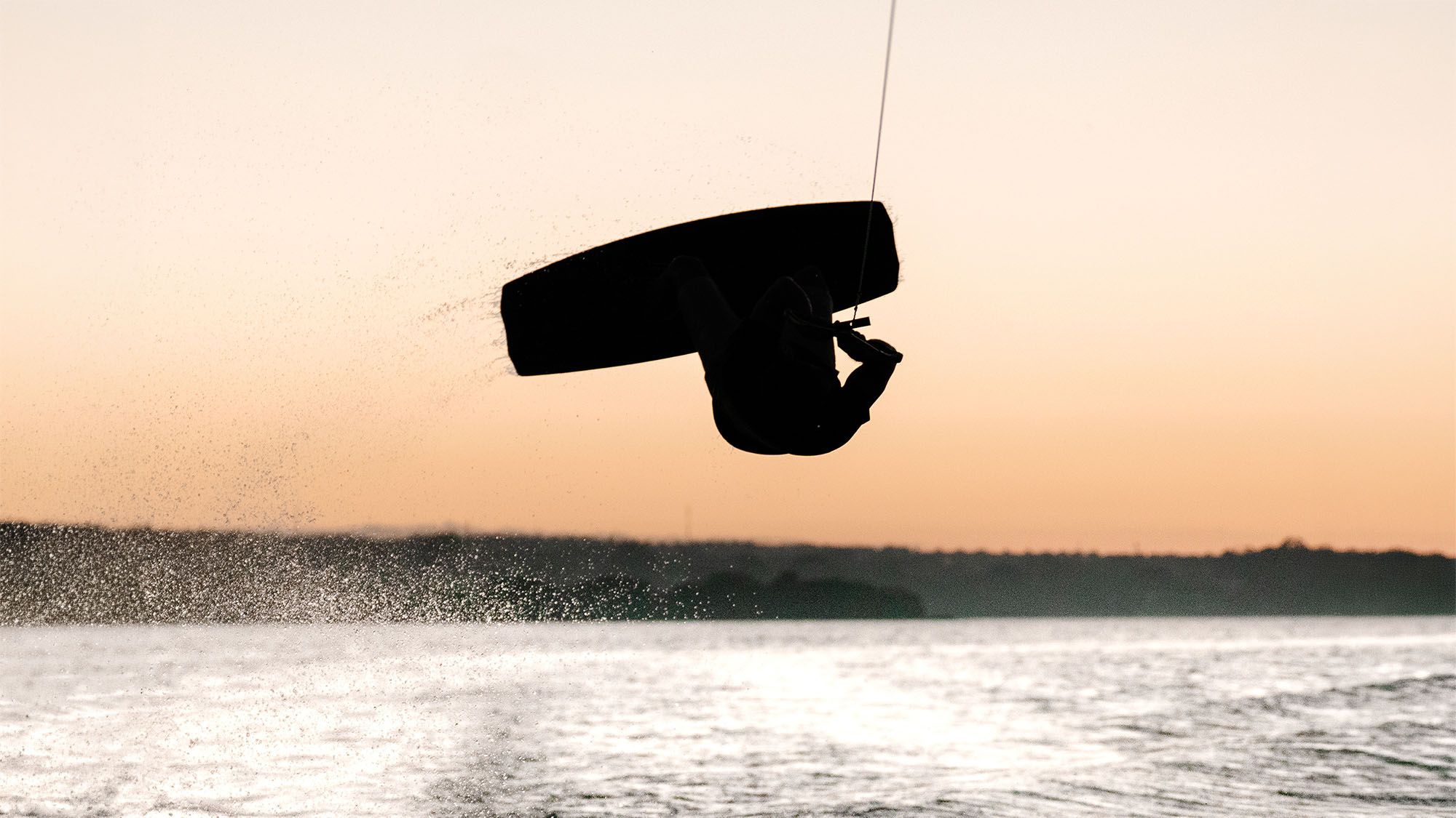 Silhueta de um backflip de wakeboard contra o céu alaranjado do pôr do sol