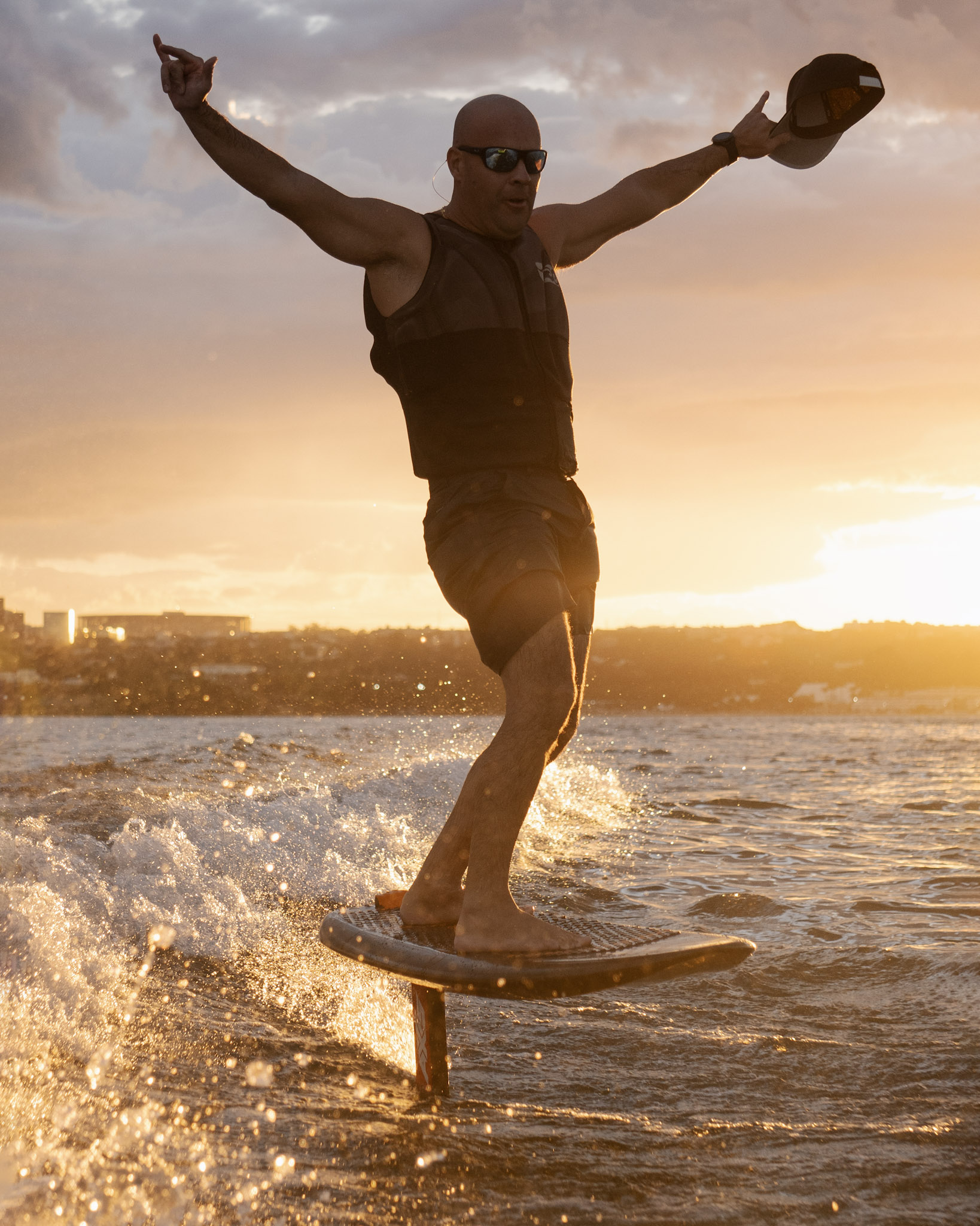 Rider de braços abertos voando na prancha de foil no pôr do sol do Lago Paranoá