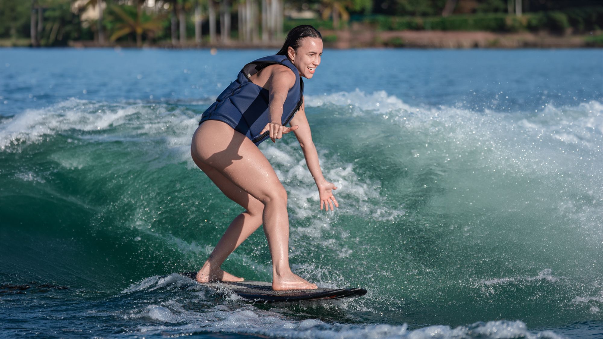 Aluna sorrindo em pé na prancha de wakesurf, surfando a onda verde da lancha