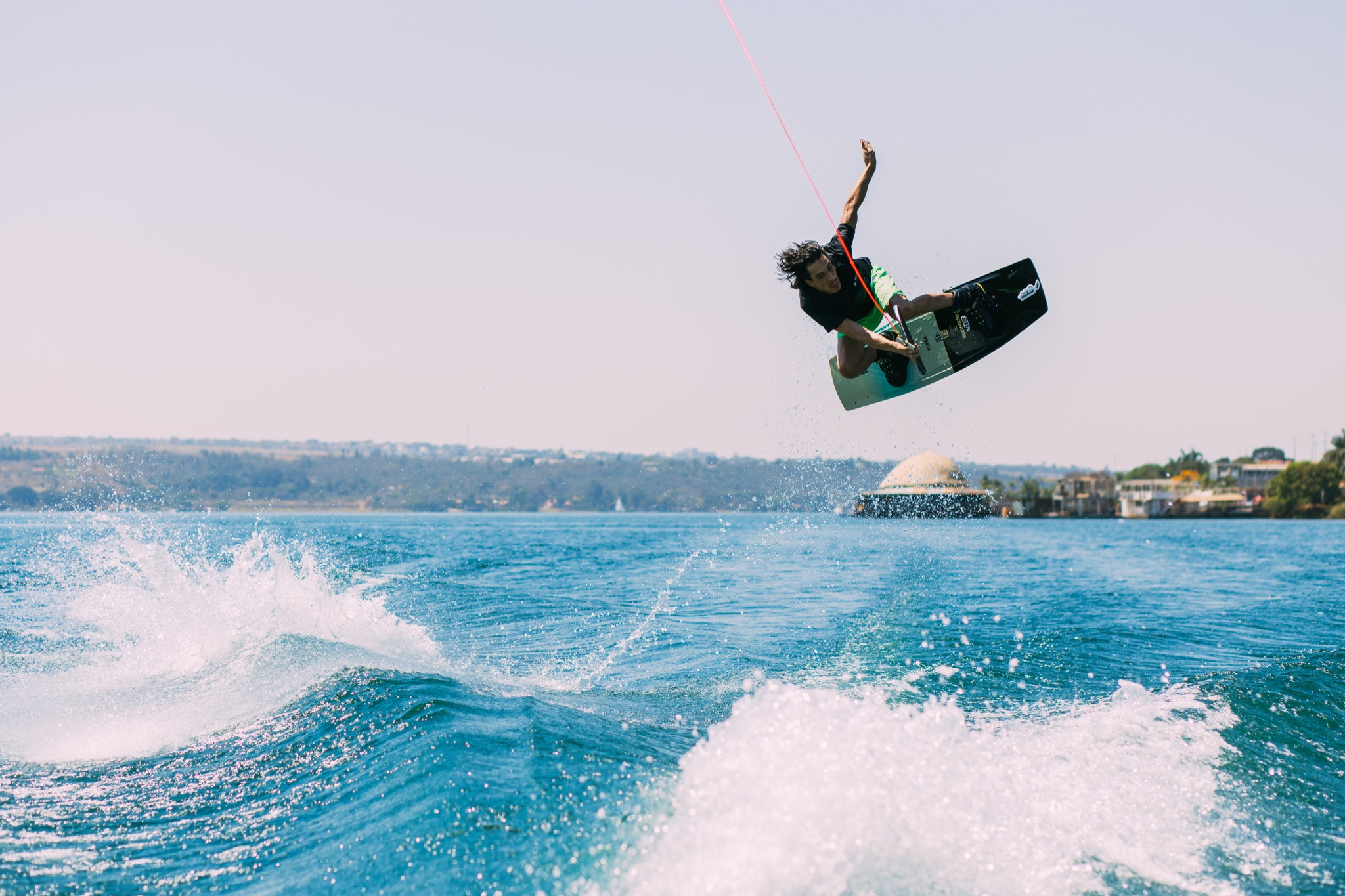 Wakeboarder alto no ar num grab sobre a esteira azul do Lago Paranoá