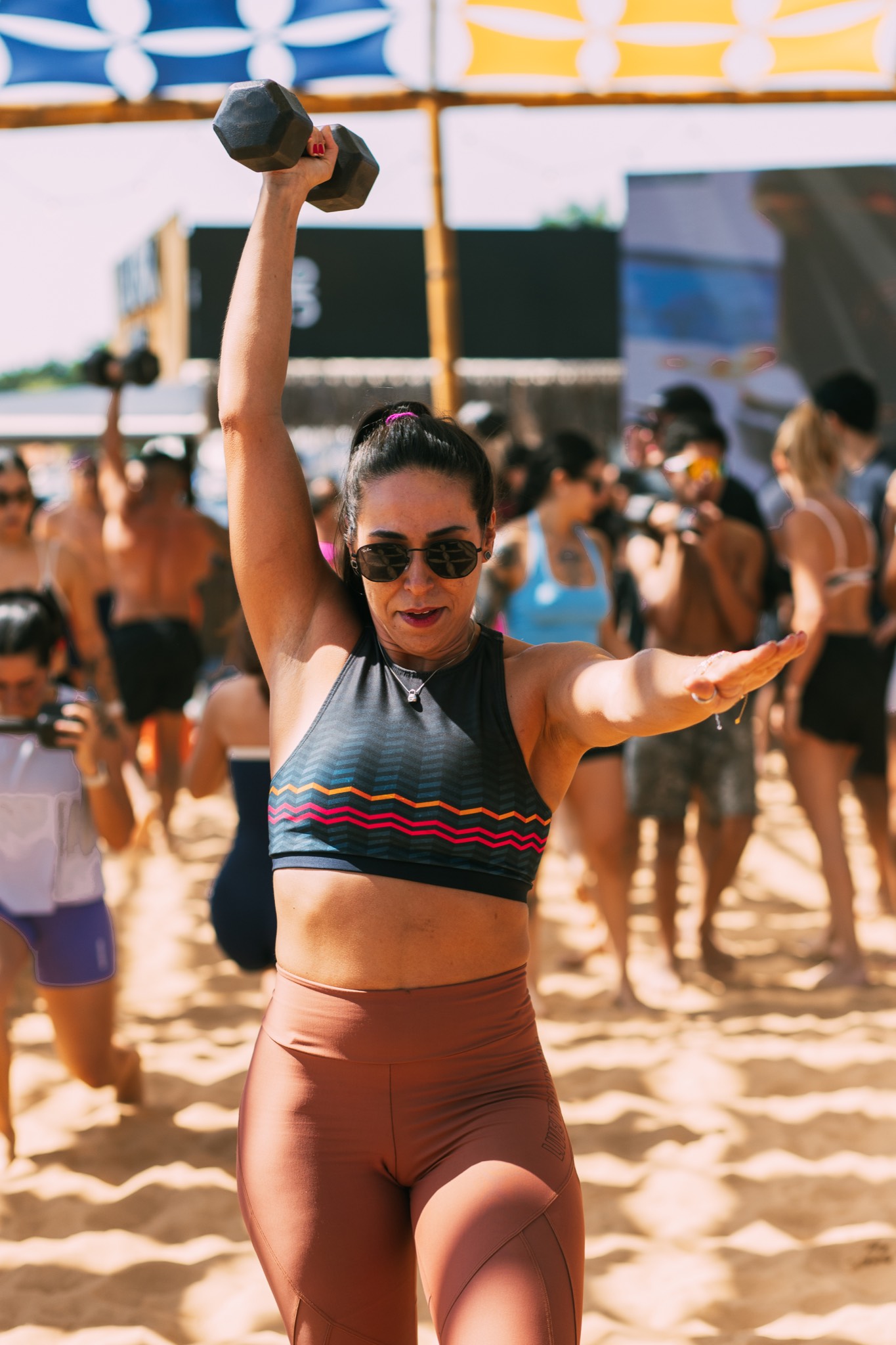 Atleta em pé com halter erguido no treino funcional na areia do Lake Deck