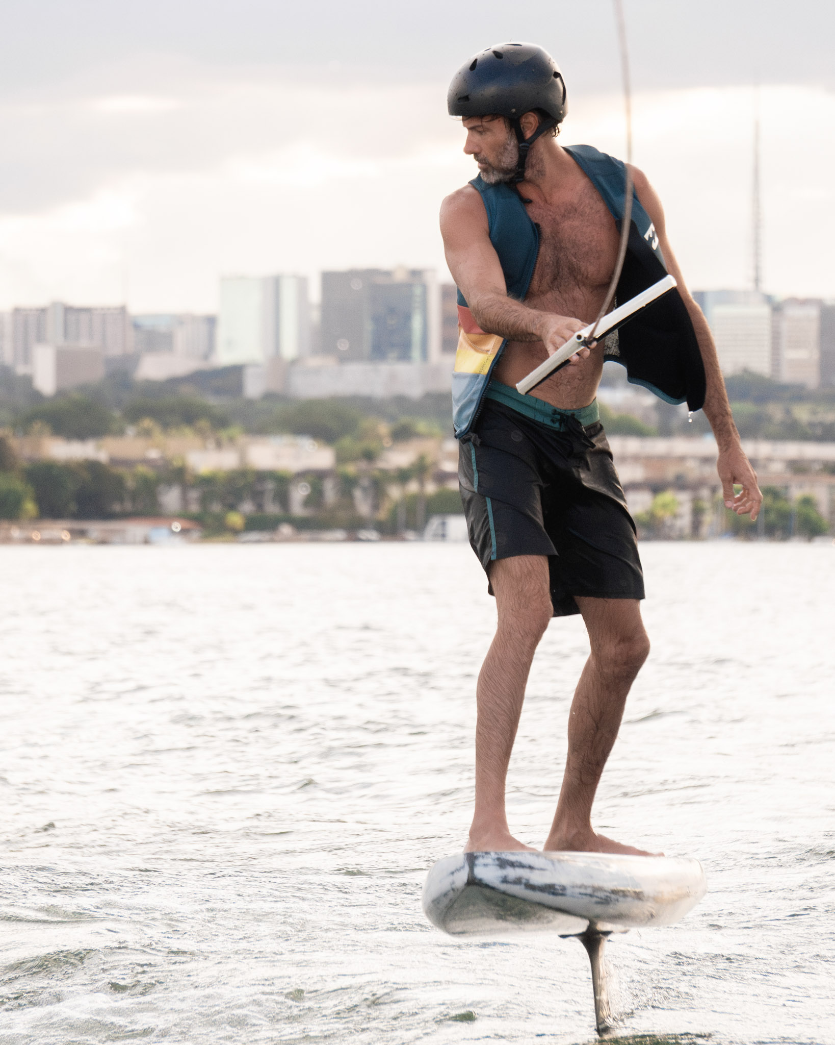 Rider de capacete voando na prancha de wakefoil, com o skyline de Brasília ao fundo