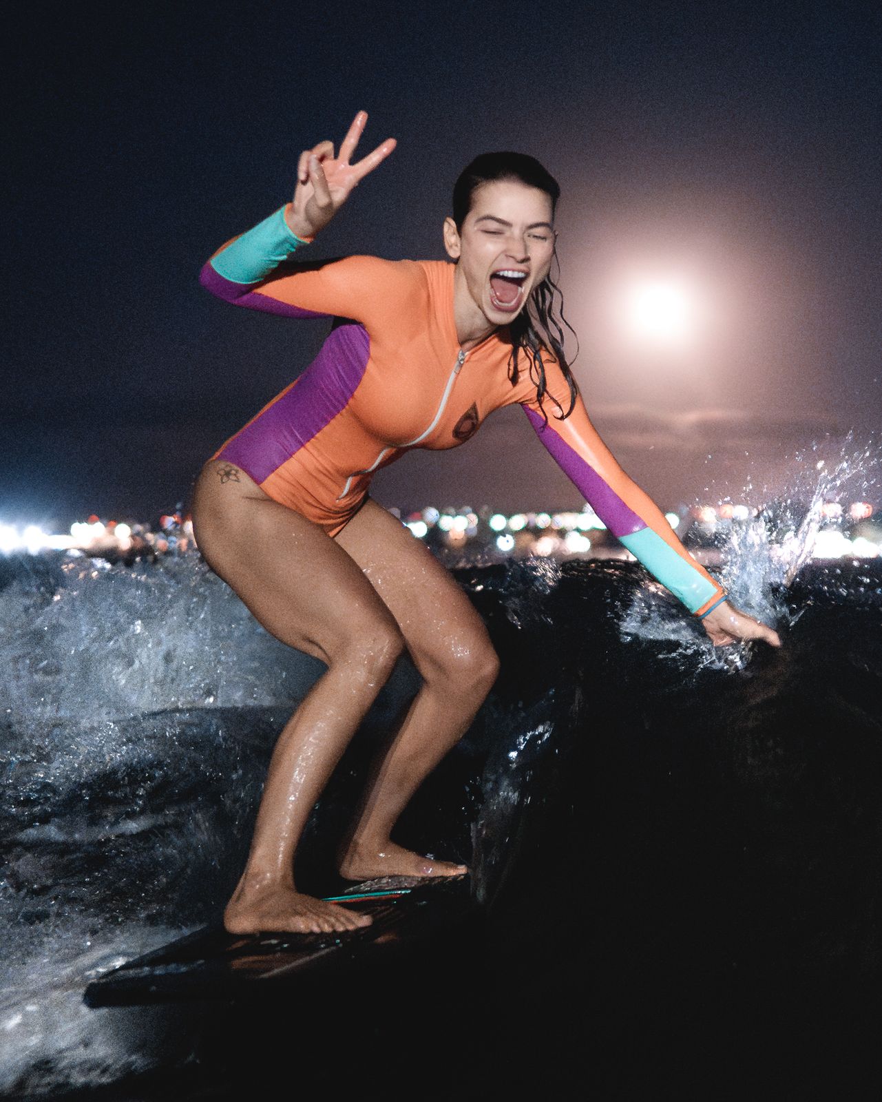 Aluna em pé na prancha de wakesurf, sorrindo e fazendo sinal de paz